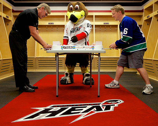 Ryan Walter (left) battles Jason Kurylo for table hockey supremacy as Hawkey looks on in the Abbotsford Heat locker room. Photo by Clint Trahan for Pucked in the Head.